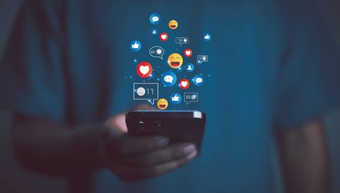 Person using smartphone with social media icons, likes, hearts, and emojis floating