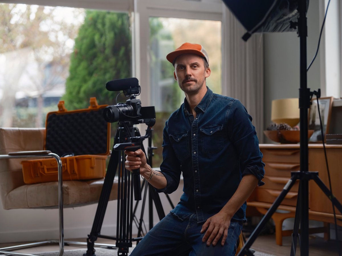 Professional filmmaker seated with camera gimbal displaying confidence in residential studio environment